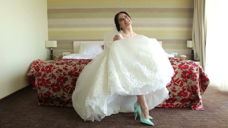 愉快的新娘坐床在旅馆显示她美丽的鞋子